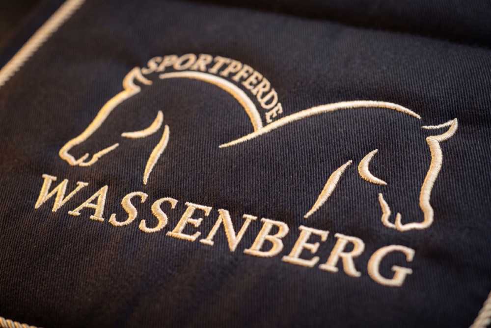Nahaufnahme: Wappen Sportpferde Wassenberg, in Creme auf Navy gestickt